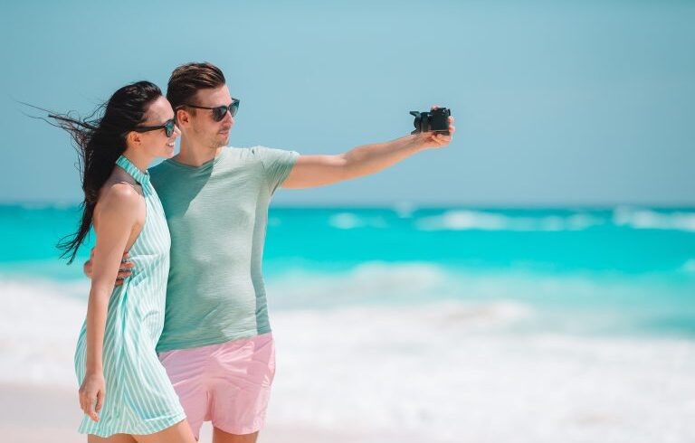 happy-couple-taking-a-photo-on-white-beach-on-hone-2021-08-27-14-37-09-utc-min-768×512